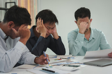A team of tired, stressed young businessmen hold their heads in their hands. From working with...
