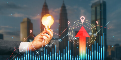 Close up of businessman hand holding lamp with growing forex chart with arrow on blurry city...