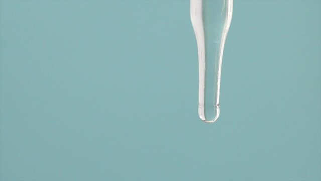Macro video of dropper & beaker on plain background. Close up of scientific lab equipments on coloured background. Drops of transparent liquid falling from top.