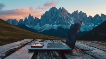 A laptop is open on a wooden table in front of a mountain range - Powered by Adobe
