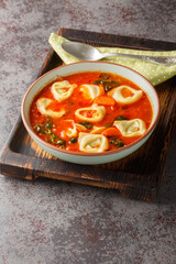 Vegetarian tomato tortellini pasta soup with vegetables and spinach close-up in a plate on the table. Vertical