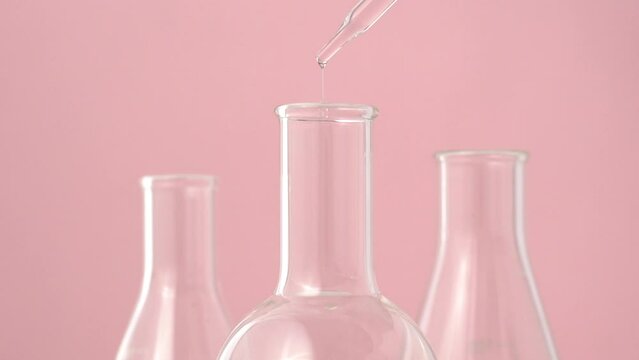 Macro video of dropper & beaker on plain background. Close up of scientific lab equipments on coloured background. Drops of transparent liquid falling from top.