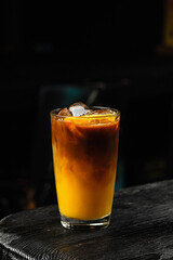 A glass of refreshing iced bumble cold coffee drink with orange juice, on wooden table