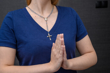 Młoda dziewczyna chrzecijanka katoliczka modli się, ma złożone ręce do modlitwy, na szyi...