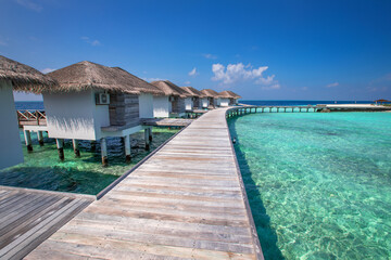 hotel water villas in Maldives, beach vacations, wooden pier and houses on pillars with straw roofs