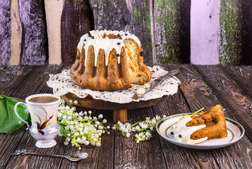 Easter cake on a wooden tray, a cup of coffee, candles, a bouquet of fragrant lily of the valley...