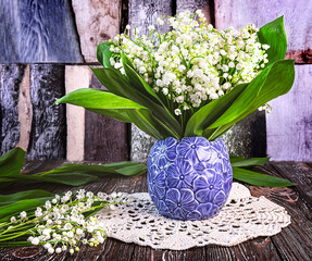 A bouquet of fresh lily of the valley flowers in a blue vase on a dark wooden background. Spring...