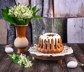 Easter cake on a wooden tray, Easter eggs, a bouquet of fragrant lily of the valley flowers on a...