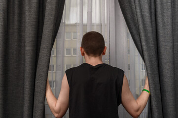Wścibski facet ogląda osiedle przez zasłonięte okno 