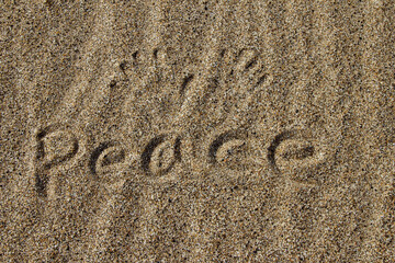 The word PEACE in English. The beautiful word peace is written on the sandy coast. Conceptual inscription on shiny sand and a beautiful seascape background. A word drawn on the beach.