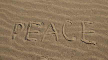 The word PEACE in English. The beautiful word peace is written on the sandy coast. Conceptual inscription on shiny sand and a beautiful seascape background. A word drawn on the beach.
