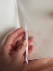 Vertical close up shot of woman’s hand holding a white bookmark ribbon of an open notebook with...