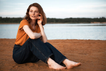 Red-haired girl in an orange T-shirt on the shore of a lake. Grain effect used