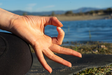 Woman's hand doing the gyan mudra in nature with a lake behind