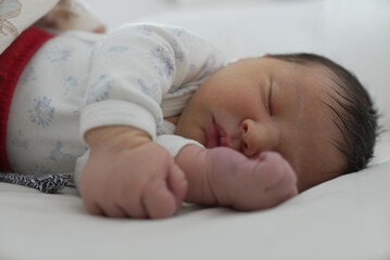 Serene image of a newborn baby sleeping on a white bed, with emphasis on the small hand and foot....