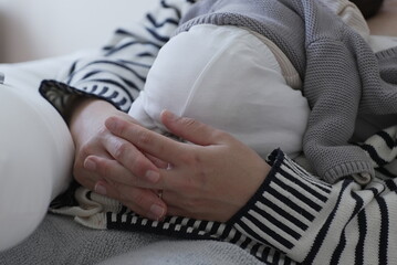A mother gently holds her newborn baby, who is wrapped in a cozy gray sweater and resting...