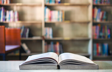 An open book or textbook vintage style on wooden table in the library and the bookshelves...