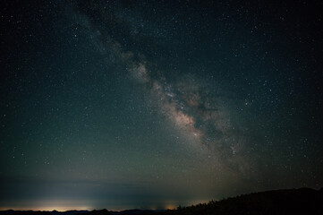 Fototapeta premium 流れ星と共に輝く天の川、森のシルエットが浮かぶ夜空