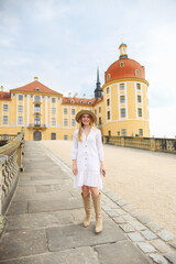girl in a white dress, beige boots and a beige hat near Moritzburg Castle