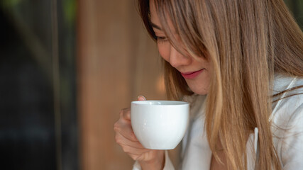 Banner of Asian woman holding hot coffee in paper mug cup to sniff smell of espresso in morning sunlight. girl carry coffee break to sniff fragrant smell the aroma of coffee.