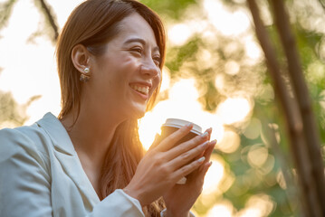 Asian woman holding hot coffee in paper mug cup to sniff smell of espresso in morning sunlight....