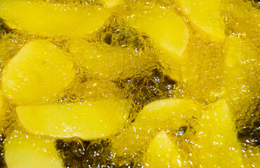 Primer plano de patatas friéndose en aceite caliente. Trozos de patatas rodeadas de burbujas del aceite hirviendo en su proceso de elaboración. French fries.