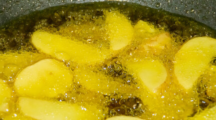 Primer plano de patatas friéndose en aceite caliente. Trozos de patatas rodeadas de burbujas del aceite hirviendo en su proceso de elaboración. French fries.