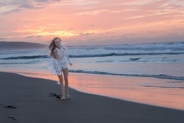 Woman enjoys a carefree run along the shoreline with a radiant sunset backdrop, her hair flowing in...