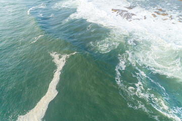 foam of the waves on the shore of a beach. Aerial view from drone