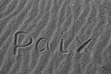 The word PEACE in French. The beautiful word peace is written on the sandy coast. Conceptual inscription on shiny sand and a beautiful seascape background. A word drawn on the beach. Black and white.