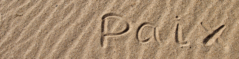 The word PEACE in French. The beautiful word peace is written on the sandy coast. Conceptual inscription on shiny sand and a beautiful seascape background. A word drawn on the beach.