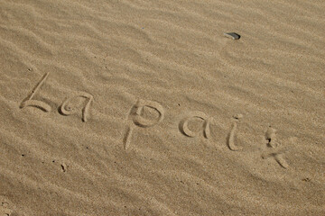 The word PEACE in French. The beautiful word peace is written on the sandy coast. Conceptual inscription on shiny sand and a beautiful seascape background. A word drawn on the beach.