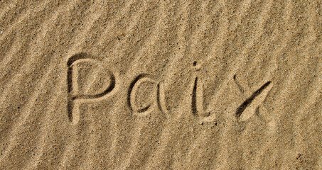 The word PEACE in French. The beautiful word peace is written on the sandy coast. Conceptual inscription on shiny sand and a beautiful seascape background. A word drawn on the beach.