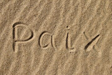 The word PEACE in French. The beautiful word peace is written on the sandy coast. Conceptual inscription on shiny sand and a beautiful seascape background. A word drawn on the beach.