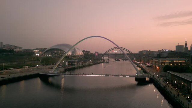 NEWCASTLE/UK 6th SEPTEMBER 2023: Drone tracks around Millennium Bridge Newcastle with Sage Centre and Tyne Bridge in background. Shot in evening twilight. A boat passes under bridge 