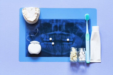 Top view of dental x-ray, jaw cast for making dental crown, pain pills and oral care products on blue background. Concept of timely dental treatment. Dental floss, brush, toothpaste. Flat lay, closeup