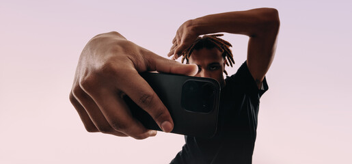 Young man capturing a self portrait with a smartphone selfie camera in a studio background