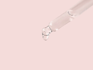 Glass pipette filled with cosmetic serum close-up isolated on pink background