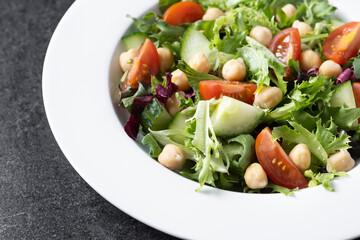 Healthy chickpea salad with tomato,lettuce and cucumber on black slate background. Close up