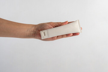Plastic white tube for cream or lotion. Skin care or sunscreen cosmetic with hand on white background.