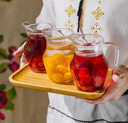 Person presents three pitchers of refreshing fruit-infused water on a wooden tray