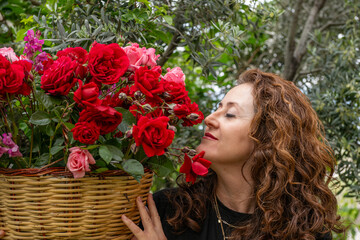 A happy woman holding a basket of red and pink roses.