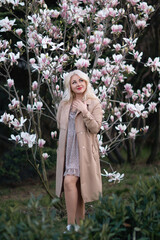 Magnolia flowers woman. A blonde woman wearing a hat stands in front of a tree with pink magnolia...
