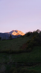 Vertical landscape with a sunlit peak at sunset and a pink sky.