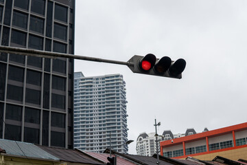 A red traffic light hangs from a pole with a background of tall, modern high-rise building.