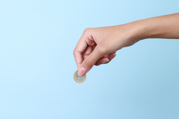 Woman hand holding a coin isolated on blue background