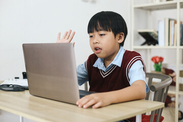 Little boy waving hand to laptop doing online class at home