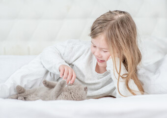 Happy little girl petting tiny kitten on the bed at home