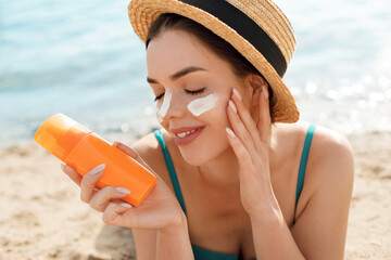 The girl uses a sunscreen for her skin. Portrait of a female holding suntan lotion and moisturizing...