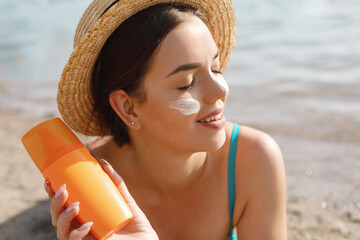 Beautiful woman applying cream sunscreen on tanned face. Sun cream. Skin and body care.
